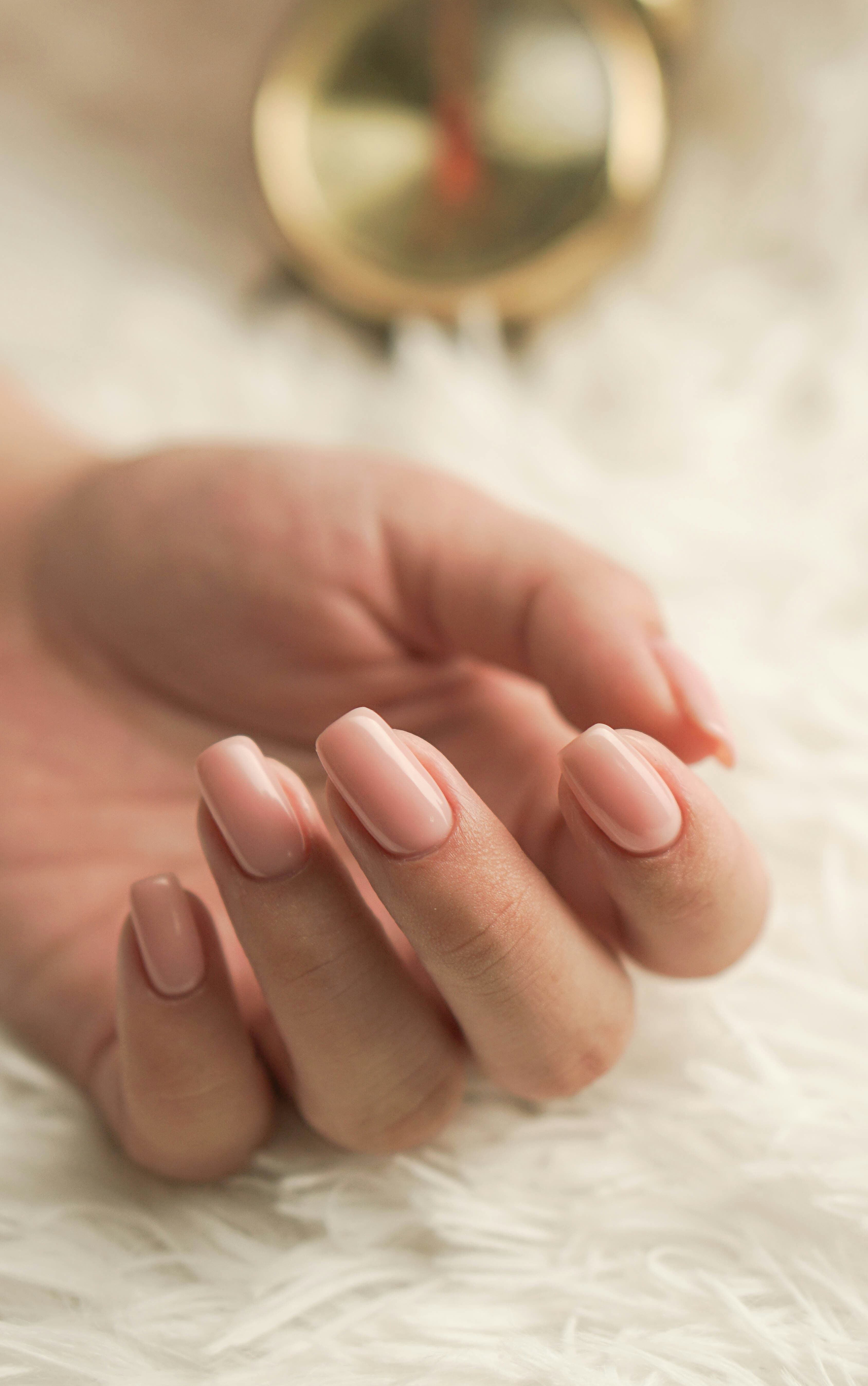 Close-cropped manicure: hand with soft pink polished nails resting on a pale surface